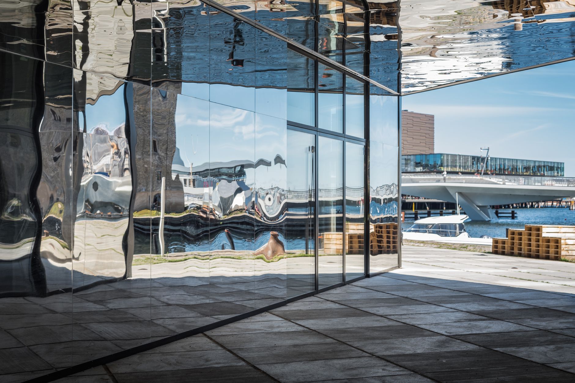 Modern architecture reflecting urban waterfront scenery in Copenhagen, featuring distorted reflections in glass surfaces.