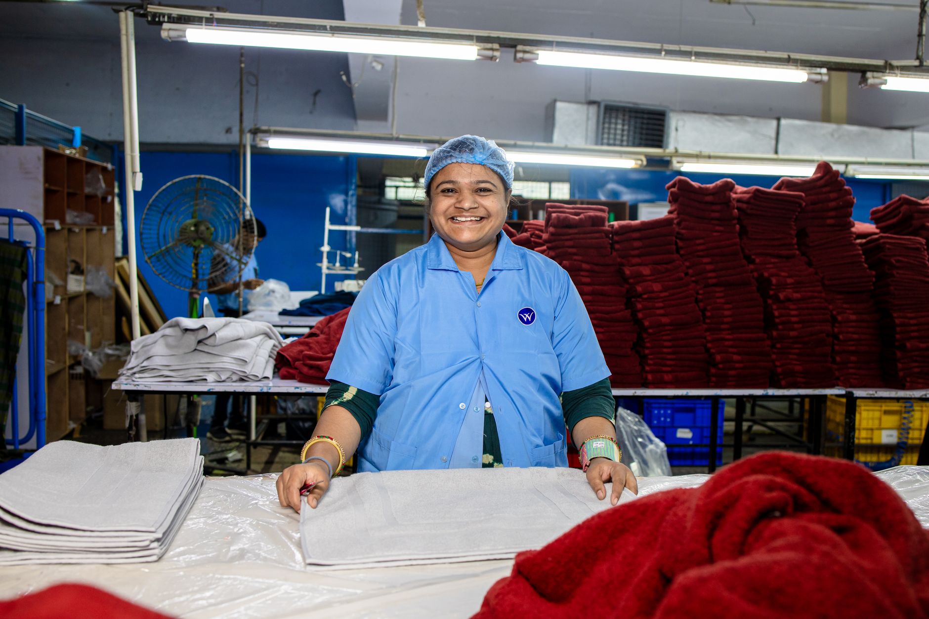 Happy factory worker folds textiles in an organized warehouse setting, showcasing textile industry efficiency.