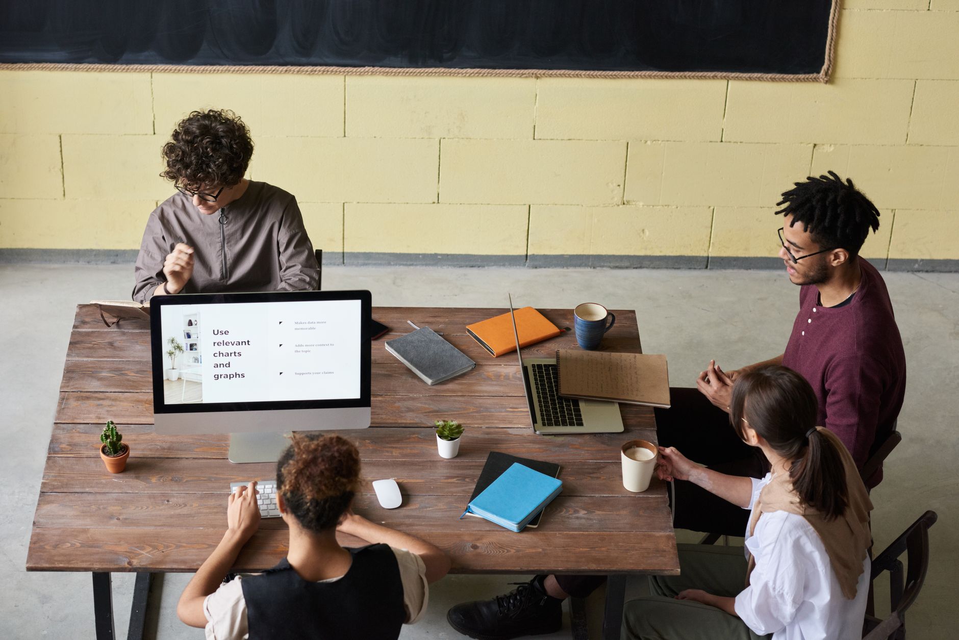 Four diverse colleagues engaged in a team meeting, working on laptops with coffee and notes, fostering collaboration.