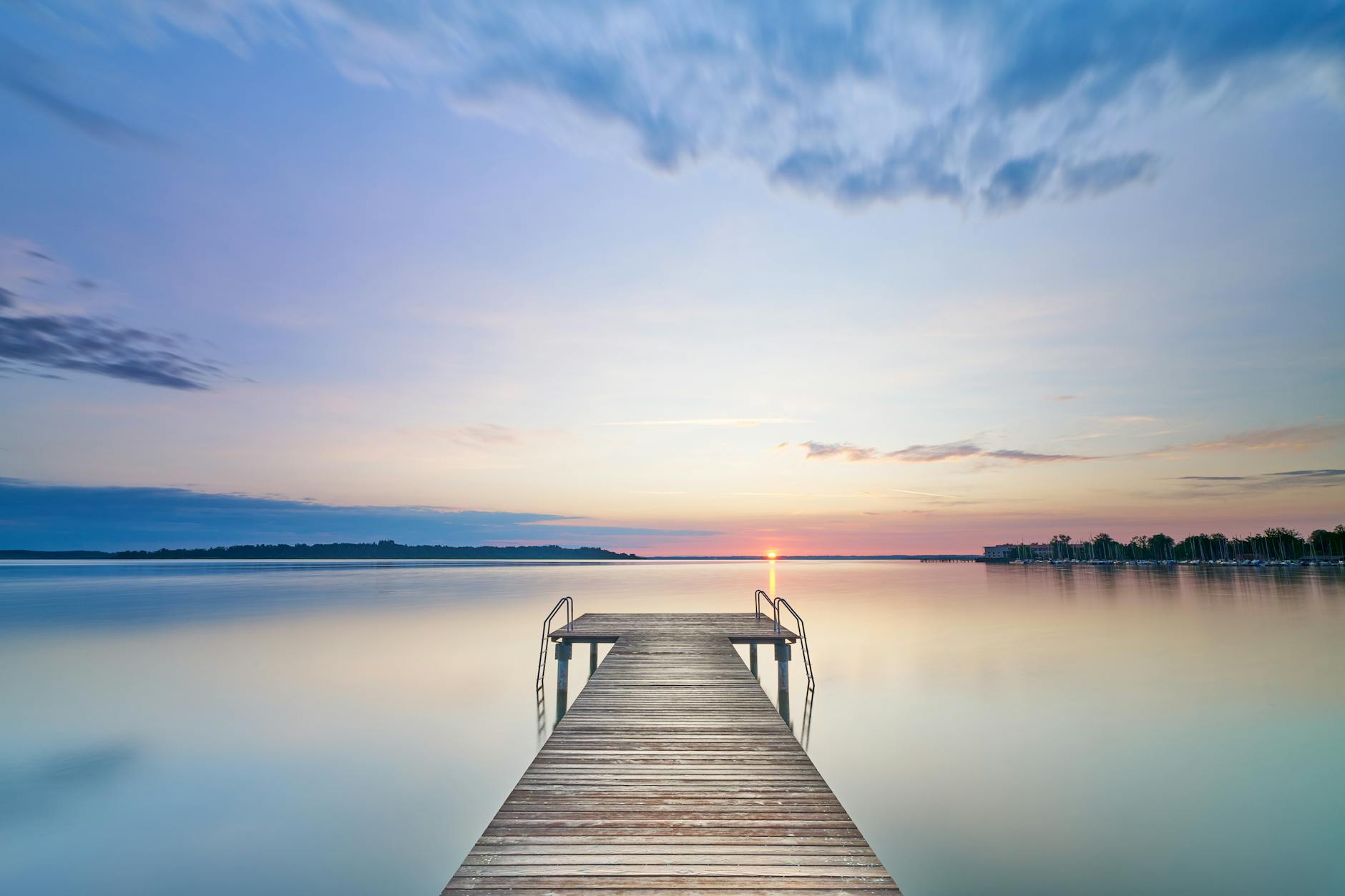 Tranquil sunrise over a wooden pier on a Bavarian lake, capturing calm reflections.