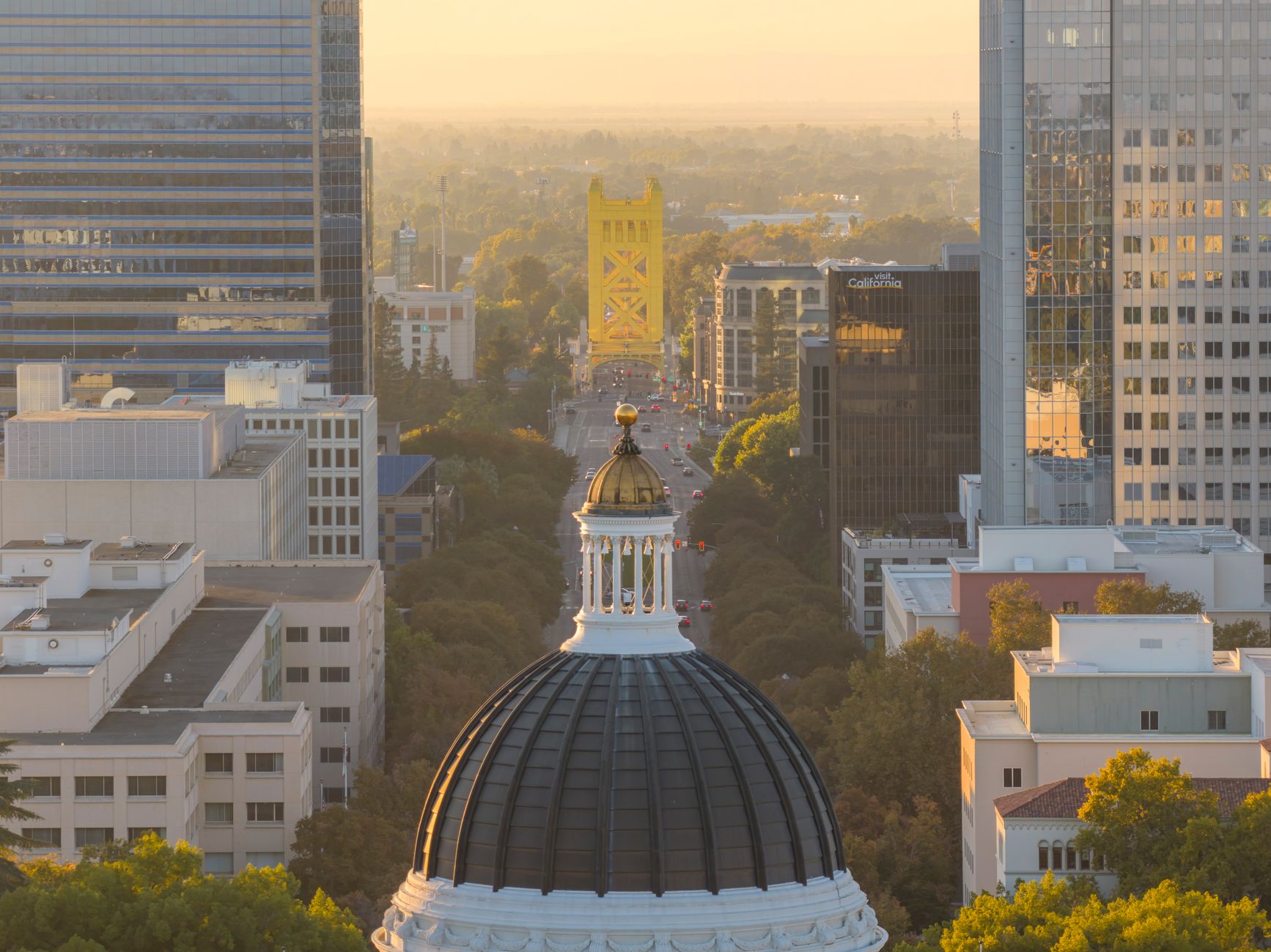 Aerial view of Sacramento skyline highlighting the Capitol Dome and iconic Tower Bridge in warm sunset light.